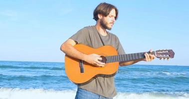 ung stilig man spelar i akustisk gitarr på stranden i solig dag, havet eller havet på bakgrunden foto
