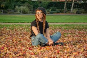 ung kvinna med röda dreadlocks och glasögon avkopplande i höstparken foto