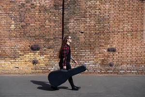 ung man med långt hår och tatuering spelar på akustisk gitarr utomhus på gatan foto
