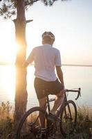 cykelryttare på professionell cykelcross cykeltur nedförsbacke, tall och sjö bakgrund foto