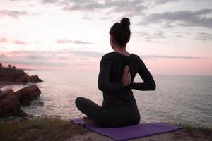 vältränad kvinna gör yoga stretching övning utomhus i vackra bergslandskap. hona på klippan med hav och soluppgång eller solnedgång bakgrund utbildning asans. siluett av kvinna i yogaställningar foto