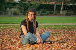 ung kvinna med röda dreadlocks och glasögon avkopplande i höstparken foto