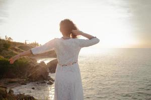 ung kvinna som går på morgonstranden i vacker vit klänning. fit hona har bra tid under turing soluppgången. foto