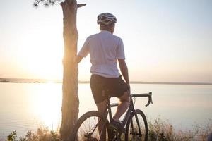 cykelryttare på professionell cykelcross cykeltur nedförsbacke, tall och sjö bakgrund foto