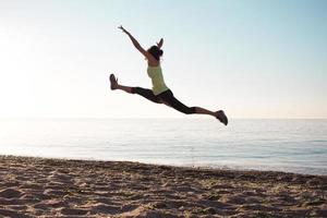 ung professionell gymnastkvinna dansar på stranden, träningsövningar med coola junps, soluppgång i havet eller havets bakgrund foto