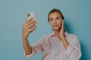 vacker kvinna med ömt uttryck tittar på smartphone kamera tar selfie av sig själv bär foto