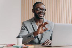 ung positiv tillfredsställd afroamerikansk affärsman i kostym pratar med affärspartner online foto