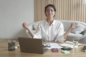 attraktiv kvinnlig entreprenör sitter i avslappnad position vid skrivbordet framför laptop med slutna ögon foto