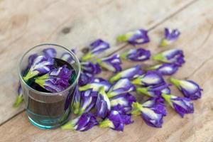 lila fjärilsärtblommor i ett glas på ett trägolv. foto