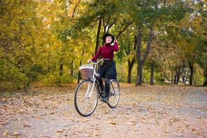 ung kvinna i höstparken läsa bok, vacker rödhårig kvinna med cykel på det gröna gräset foto