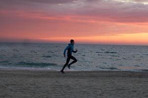 ung man i atumn kläder träning på stranden, soluppgång bakgrund, manlig löpare på morgonen foto