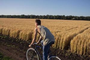 ung man rida fast växel cykel på landsvägen, fält och blå himmel bakgrund foto