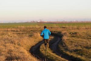 ung man trail runner utbildning utomhus på fälten, solnedgång i sjön bakgrund foto