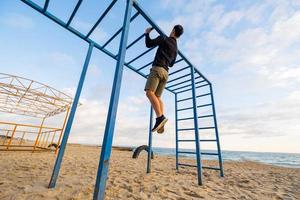 unga vältränade manliga träning gör övningar utomhus på stranden foto