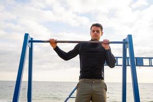 unga vältränade manliga träning gör övningar utomhus på stranden foto