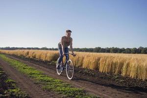 ung man rida fast växel cykel på landsvägen, fält och blå himmel bakgrund foto