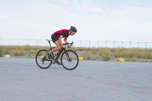 cykelracer i hjälm och sportkläder träning ensam på tom landsväg, fält och träd bakgrund foto