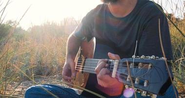 ung stilig man spelar i akustisk gitarr på stranden i solig dag, havet eller havet på bakgrunden foto