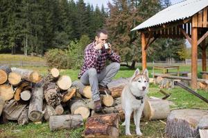 turist kopplar av på hugget ved med husky hund och dricker te eller kaffe foto