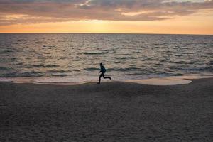 ung man i atumn kläder träning på stranden, soluppgång bakgrund, manlig löpare på morgonen foto