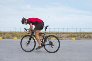 cykelracer i hjälm och sportkläder träning ensam på tom landsväg, fält och träd bakgrund foto