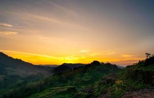 vackert naturlandskap av bergskedja med solnedgångshimmel och moln. bergsdalen i thailand. landskap av bergslager i skymningen. tropisk skog. naturlig bakgrund. orange och gyllene himmel. foto