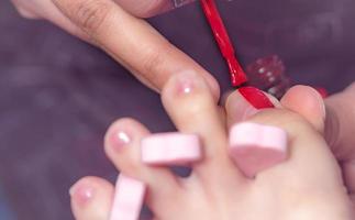 kvinna som får tånagelpedikyrservice av pedikyr på nagelsalongen. kosmetolog som applicerar röd gelfärg på tånageln på kunden på nagel- och spasalong. fotvård och tånagelbehandling på nagelsalong. foto