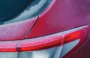 röd bil täckt av frost och is av vit snö under vintersäsongen. närbild bakifrån av röd bil parkerad på utomhus parkeringsplats. kallt och fruset väder. frost på bilens bakruta och baklykta. foto