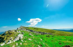 landskap av grönt gräs och rock hill på våren med vacker blå himmel och vita moln. utsikt över landsbygden eller landsbygden. natur bakgrund i solig dag. frisk luft miljö. sten på berget. foto