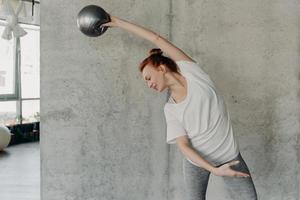 atletisk ingefärshårig ung kvinna som utför barre övning med små fitball foto
