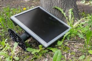 en defekt monitor ligger på gatan under ett träd i gräset foto