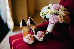 brudar skor och bröllopsbukett med mjuka blommor på röd stol. bröllopsförberedelser. bröllopstillbehör. rosa brudskor och frodig bukett i brudens rum. brudar morgon. Bröllopsfoto foto