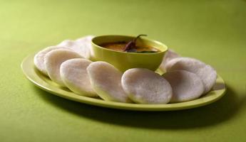 idli med sambar i skål på grön bakgrund, indisk maträtt sydindisk favoritmat rava idli eller semolina idly eller rava idly, serveras med sambar och grön kokosnötchutney. foto