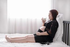asain vackra gravida kvinnor koppla av på vit säng och och dricka mjölk för god hälsa för hennes framtida barn foto