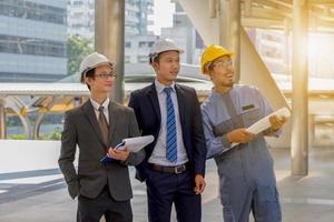 affärsingenjör hyvling med vit hjälm och håller ritpapper i handen mot stadens bakgrund hyvling och team management koncept foto