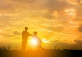 silhuett av mor och barn som leker på fältet solnedgång bakgrund, glad mor och barn koncept foto