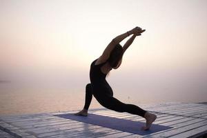 ung kvinna poserar i yoga asans, morgon havet bakgrund foto