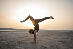 ung vältränad kvinna som tränar yogaställningar i öknen under solnedgången eller soluppgången, kvinna i svarta sportkläder gör stretchövningar foto