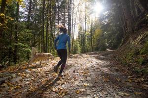 ung kvinnlig löpare utbildning i höst skog med hund foto