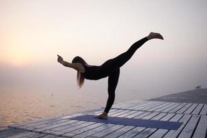 ung kvinna poserar i yoga asans, morgon havet bakgrund foto