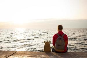 skridskoåkare med ryggsäck tittar på soluppgången eller solnedgången i havet eller havet foto