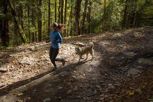 ung kvinnlig löpare utbildning i höst skog med hund foto