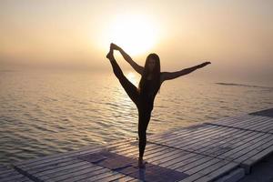 ung kvinna poserar i yoga asans, morgon havet bakgrund foto