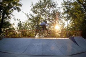 bmx ryttare tränar och gör tricks i street plaza, cykel stunt ryttare i cocncrete skatepark foto