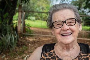 senior glad gammal bondekvinna med glasögon som ler och tittar på kameran foto