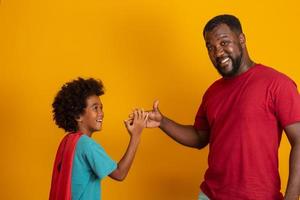 afrikansk far och son spelar superhjälte på dagtid. människor som har roligt gul bakgrund. begreppet vänlig familj. foto