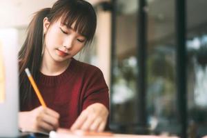 ung vuxen asiatisk college student kvinna med laptop för studier på café på vinterdag. foto