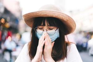 ung asiatisk resenär kvinna har nysning med mask på utomhus på dagen foto