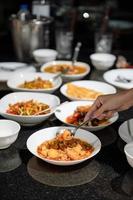 hand med sked scoop stekt tofu och olika thailändsk mat på matbordet foto