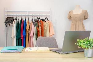online kvinnlig klädbutik med bärbar dator, anteckningsbok, dokumentfil på skrivbord och avslappnad tyg på klädstreck och skyltdocka foto